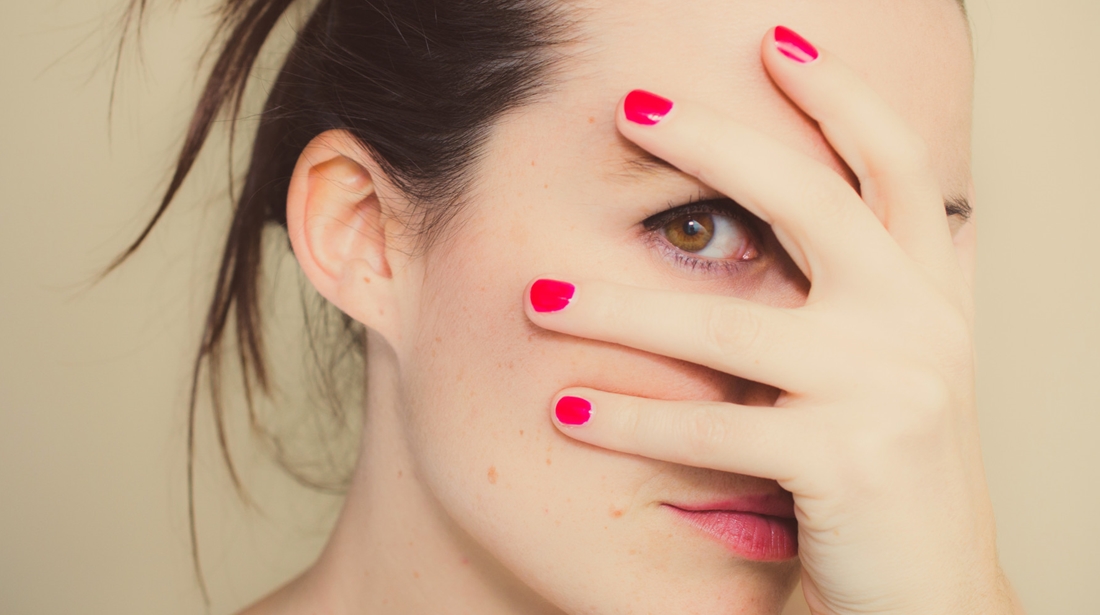Misterious girl with red nails and hand on face.